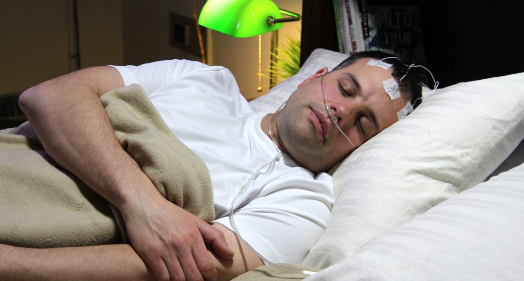 Illustrative image shows a man sleeping while connected to monitoring equipment.
