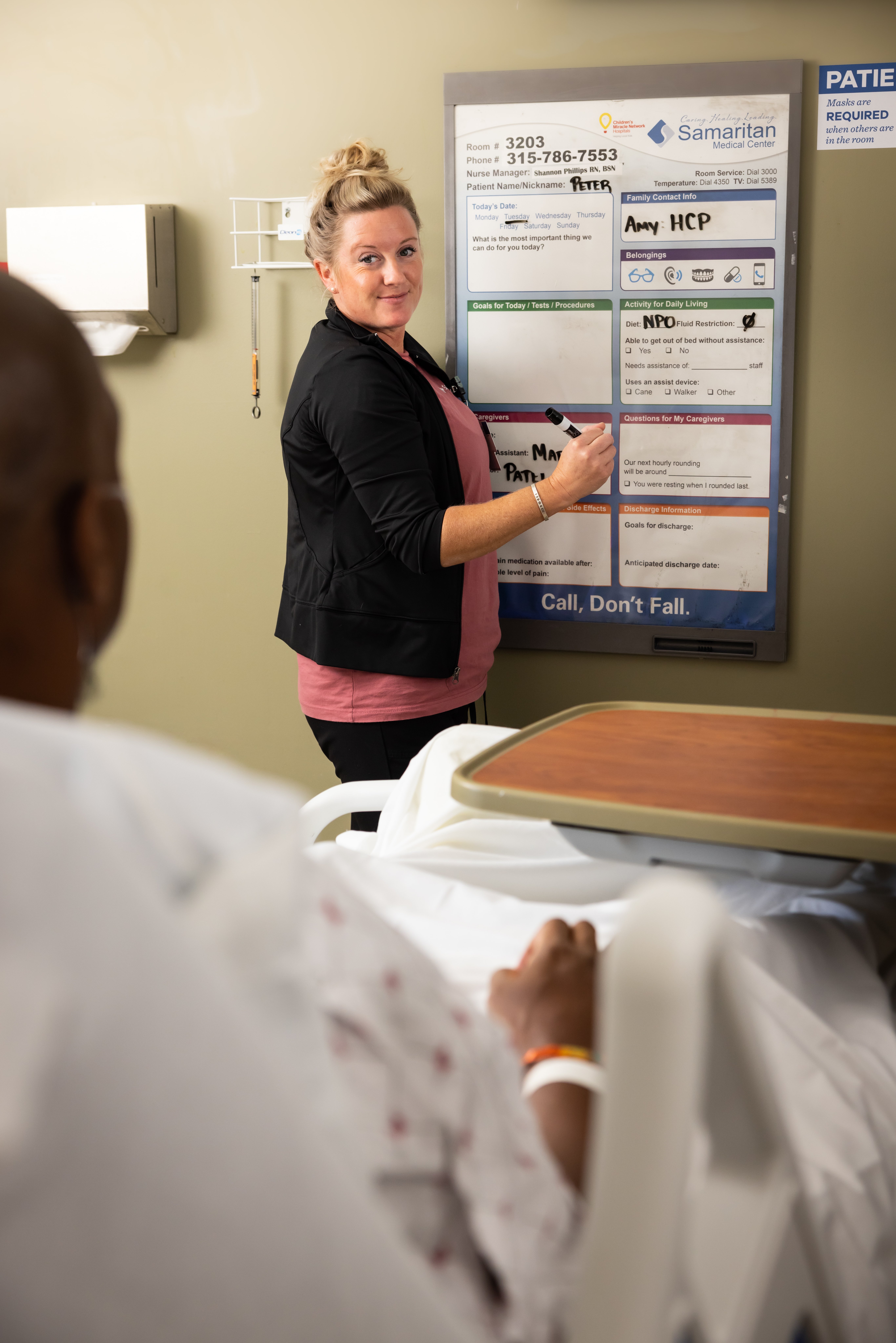 Illustrative: shows an aide helping patient with informations on the room chart.